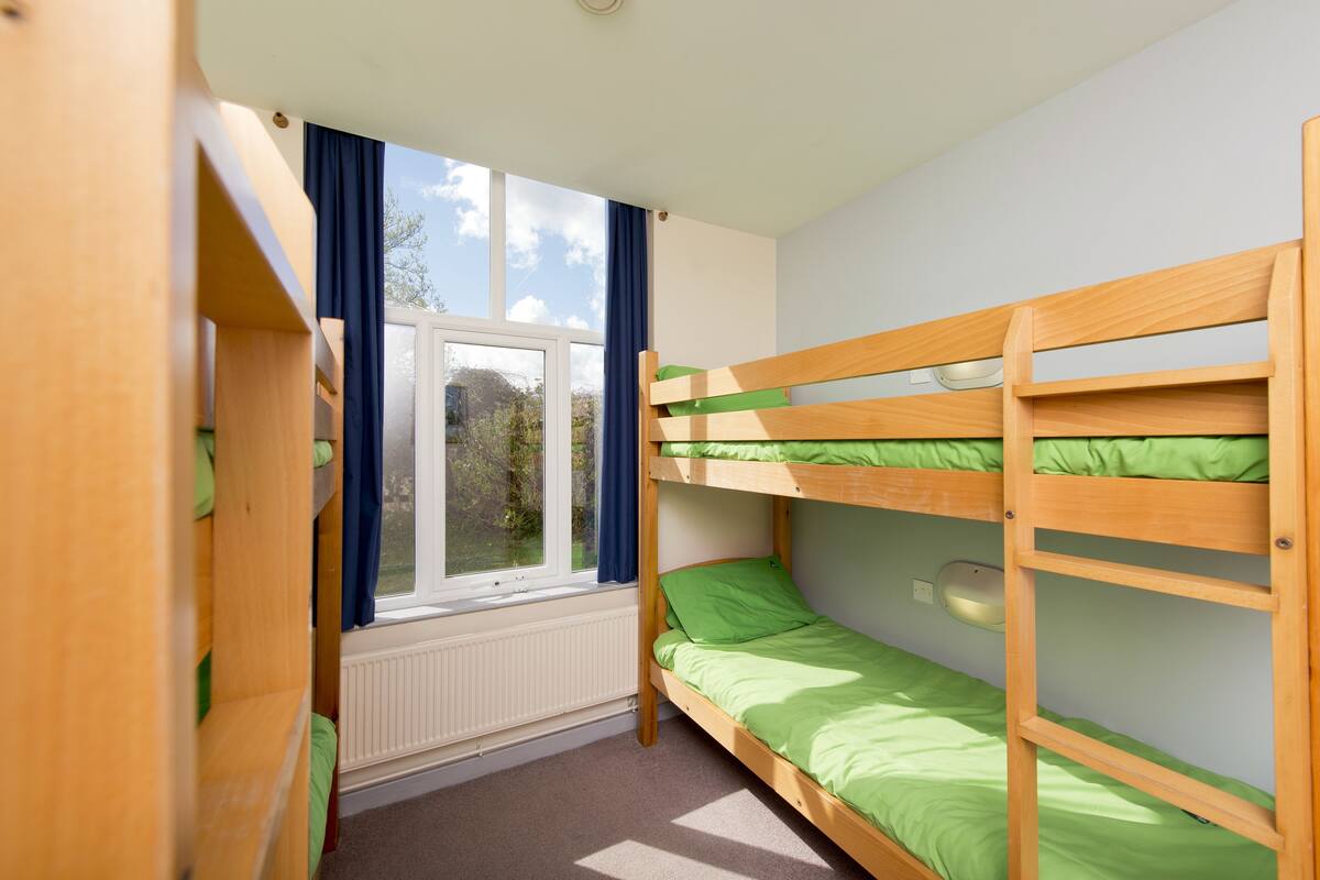 Une chambre avec des lits superposés, une fenêtre avec des rideaux et un radiateur.