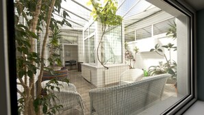 A greenhouse with wicker furniture, potted plants, and a view of the outside.