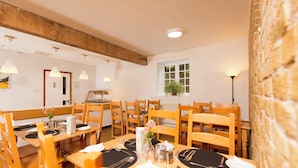 A dining area with wooden tables and chairs, a potted plant by the window, and a brick wall. - YHA Medway - Hostel (Gillingham)