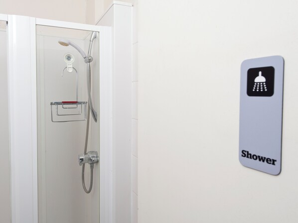 Un espace douche équipé d’un pommeau de douche, d’un pommeau de douche à main et d’un panneau fixé au mur indiquant l’emplacement de la douche.