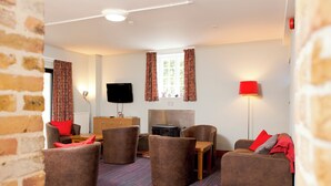 A modern living room with a flat-screen TV, comfortable seating, a fireplace, and a red lamp. - YHA Medway - Hostel (Gillingham)