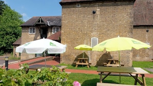 A brick building with a traditional roof, outdoor seating with umbrellas, and a grassy area with flowers. - YHA Medway - Hostel (Gillingham)