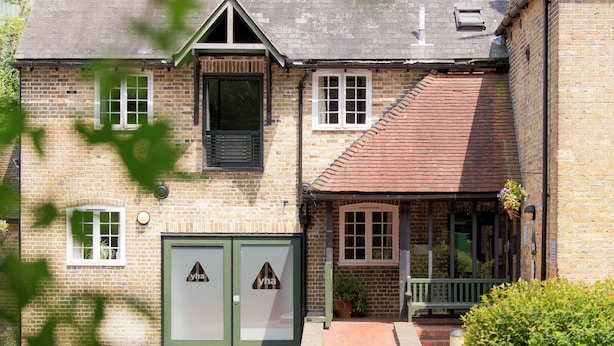 A two-story brick house with a green door, a small porch with a bench, and a window with a hanging flower basket. - YHA Medway - Hostel (Gillingham)
