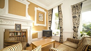 A living room with striped sofas, a wooden coffee table, a television, a bookshelf, and a fireplace. - YHA Penzance - Hostel (Penzance)