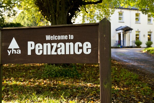 A welcome sign for Penzance with a triangular logo and the text "Welcome to Penzance" on a wooden background. - YHA Penzance - Hostel (Penzance)
