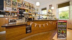 A bar area with wooden shelves stocked with various bottles, a counter with a cash register, and a promotional sign offering a drink with courses. - YHA Penzance - Hostel (Penzance)