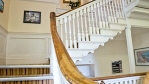 A grand staircase with white balustrades and a wooden handrail, leading to an upper floor. - YHA Penzance - Hostel (Penzance)