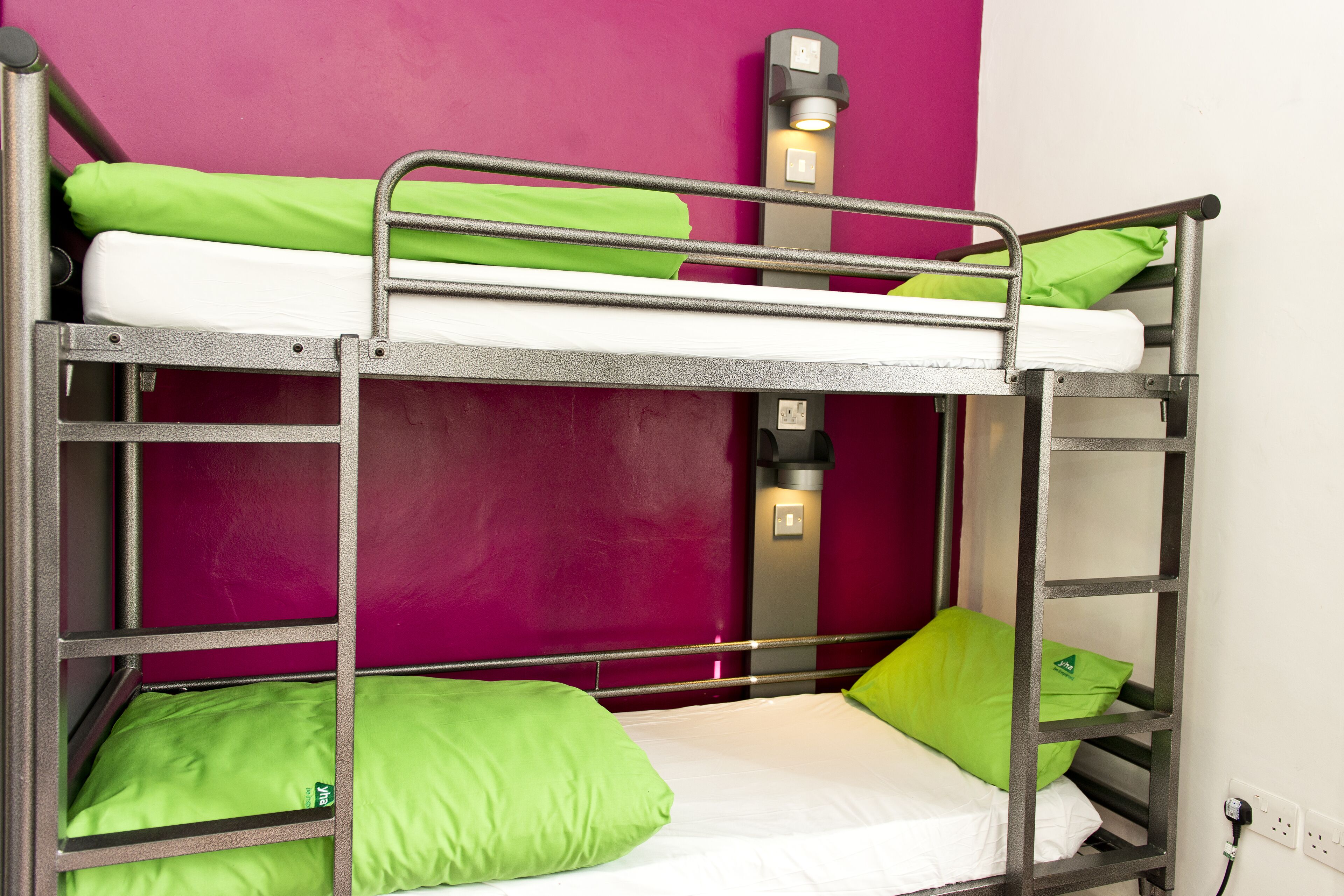Ein Stockbett mit grüner Bettwäsche und einer Wandleuchte.
