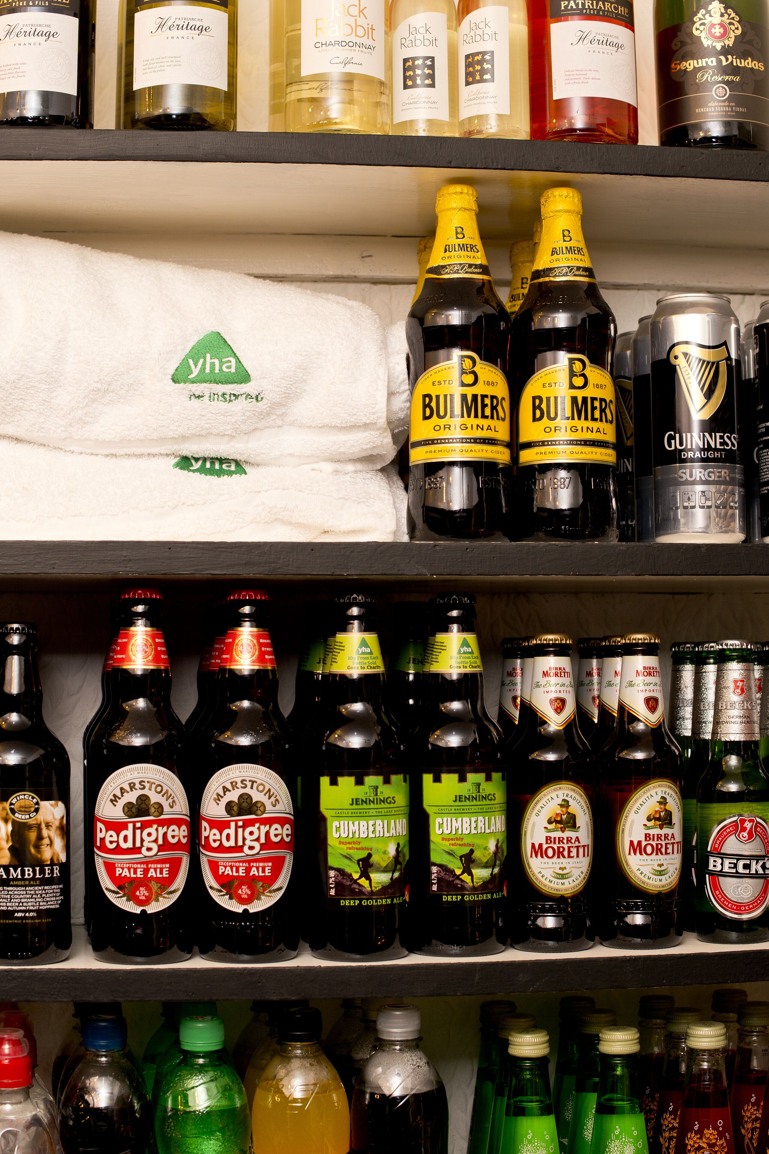 Una estantería con diversas botellas de bebidas alcohólicas, incluyendo vino, cerveza y sidra.