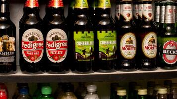 Una estantería con diversas botellas de bebidas alcohólicas, incluyendo vino, cerveza y sidra.