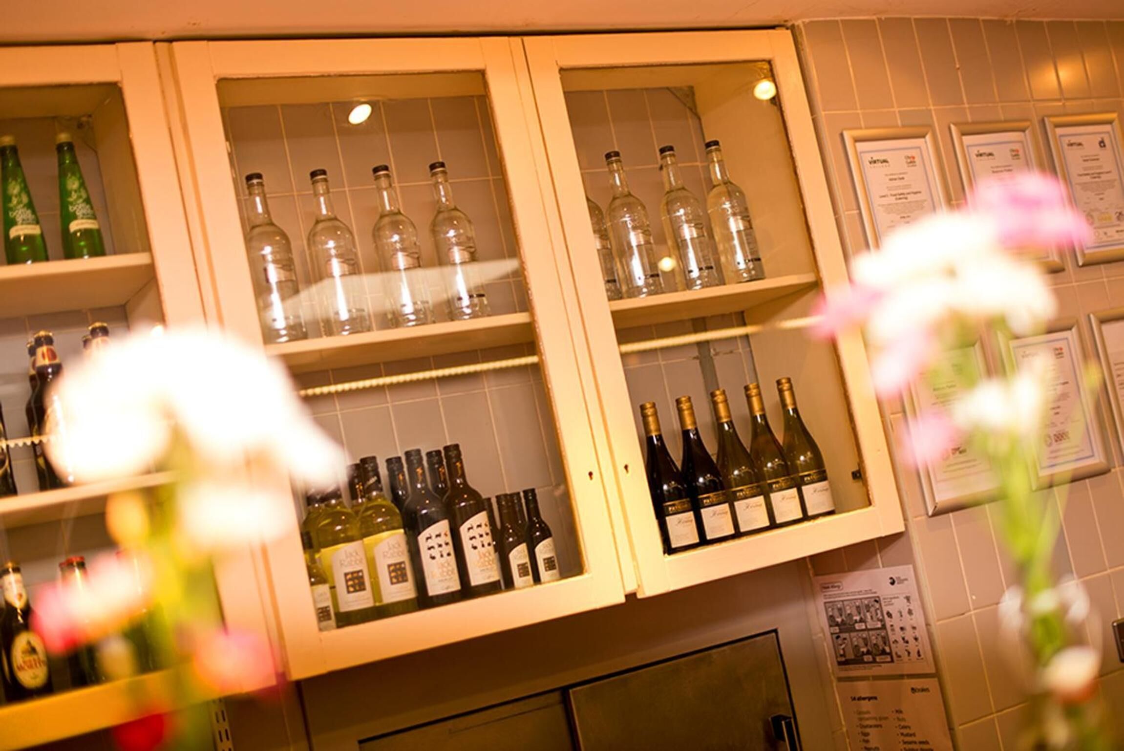 A bar area with shelves of wine bottles and glasses, and a menu board on the wall.