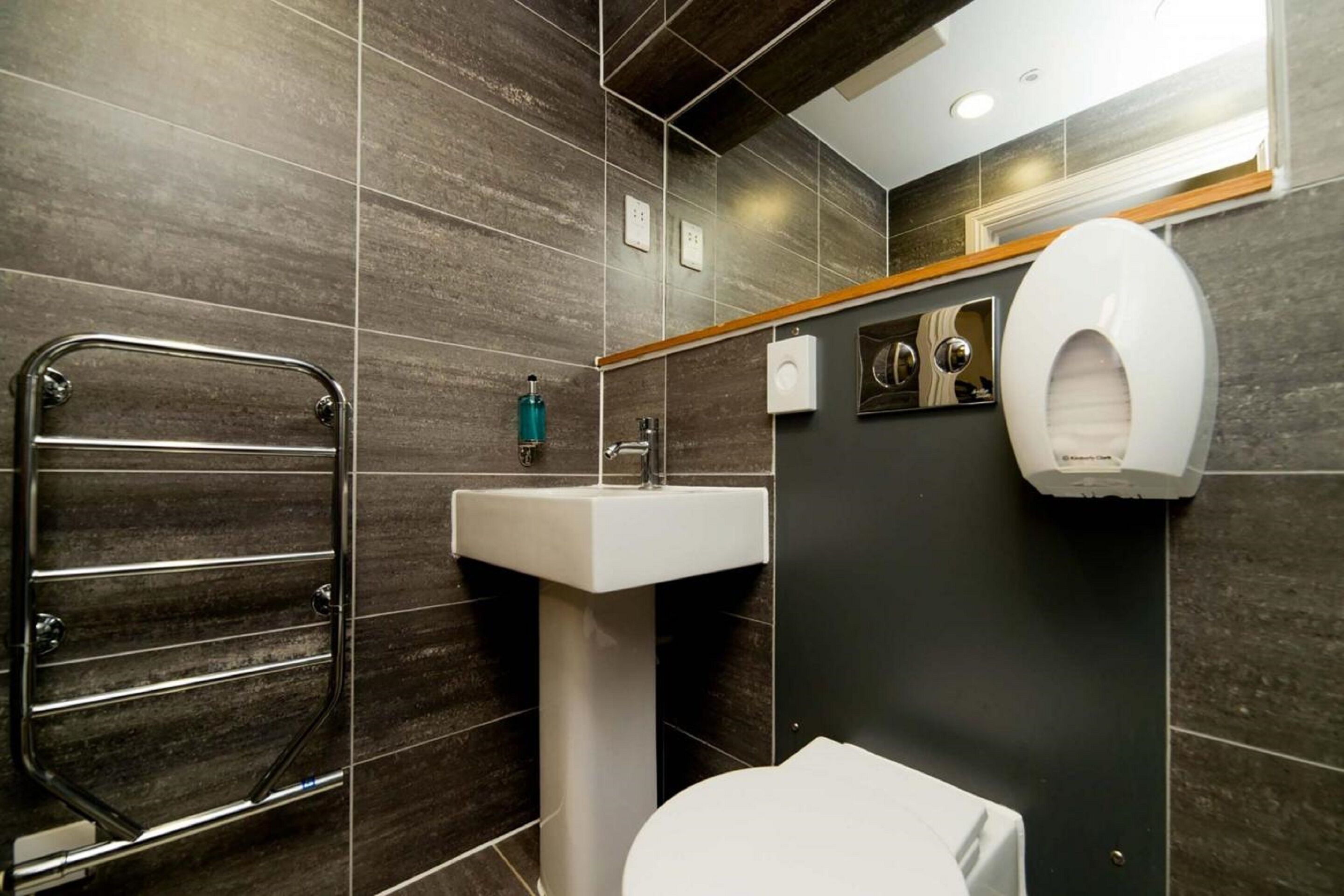 A modern bathroom with a metal towel rack, a white sink, and a toilet.