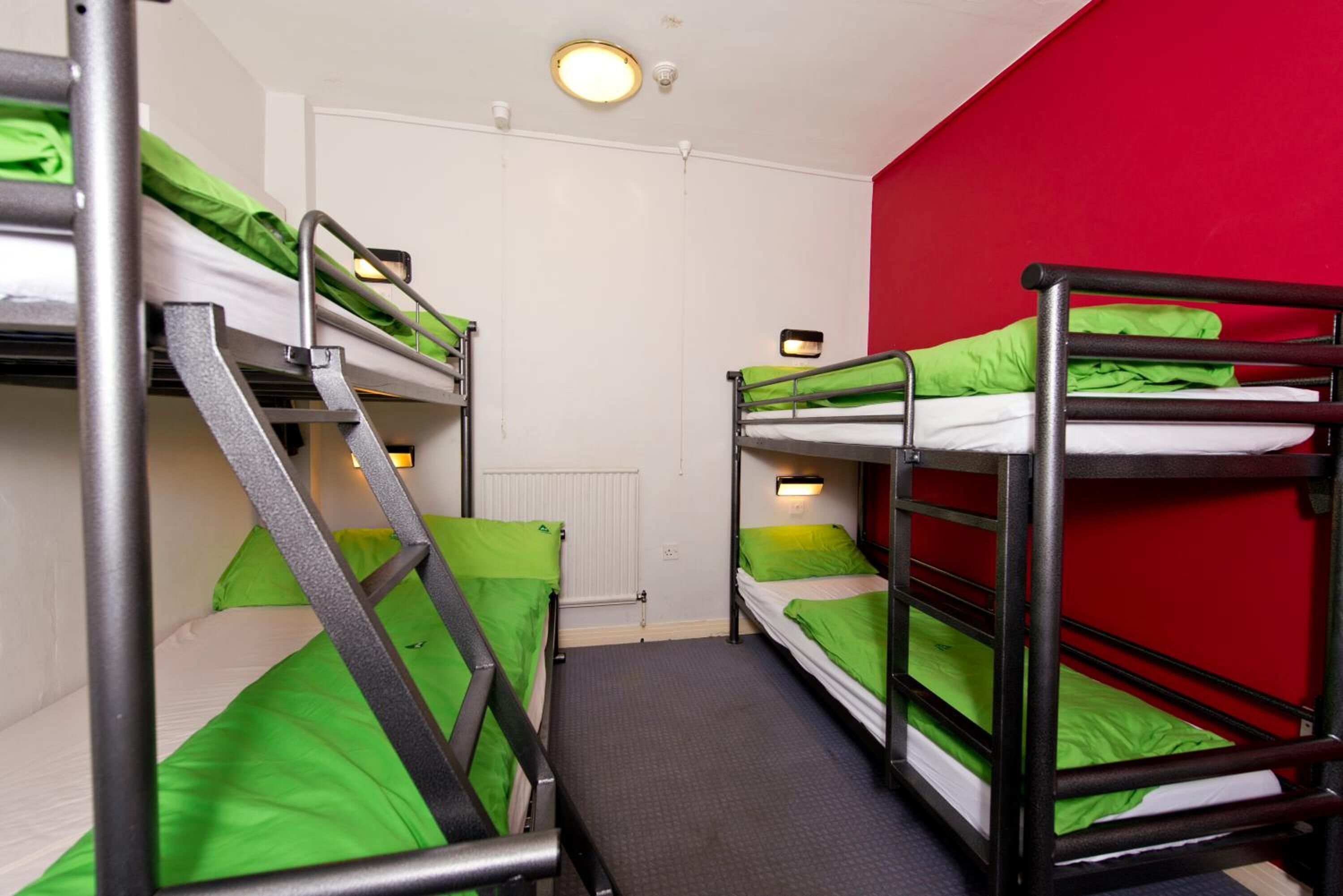 A dormitory room with bunk beds, a radiator, and a red wall.