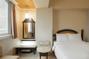 Een hotelkamer met een bed, nachtkastje, klein rond tafeltje, spiegel en raam met gordijnen.