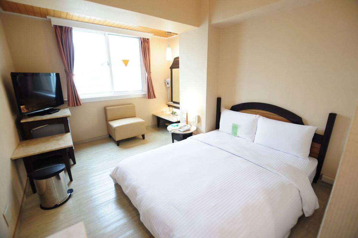 Ein Hotelzimmer mit Bett, Fernseher, Stuhl, Schreibtisch und Mülleimer.