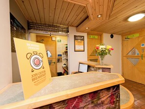 A reception area with a wooden reception desk, a sign for a morning person breakfast, and a lounge sign. - YHA Sherwood Forest - Hostel (Mansfield)