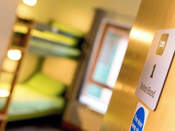 Una habitación de hotel con una cama, un letrero que indica "Puerta contra incendios, mantener cerrada" y un letrero para "Robinson Hood".