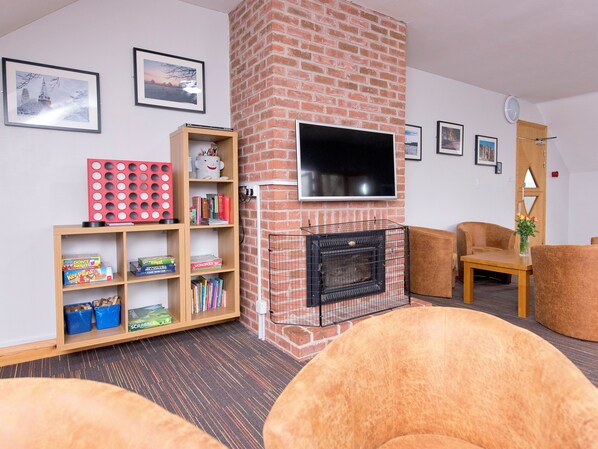A living room with a brick fireplace, a flat-screen TV, a bookshelf, and two armchairs. - YHA Sherwood Forest - Hostel (Mansfield)