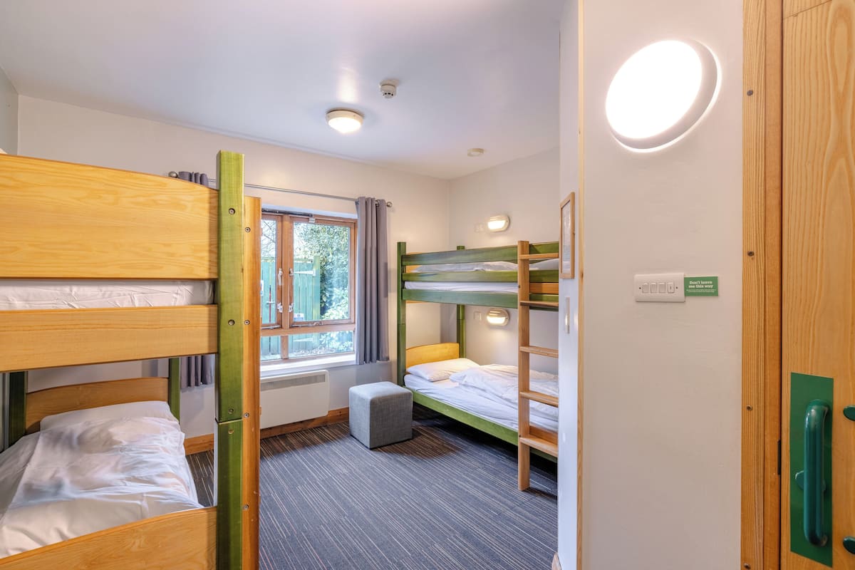 A room with bunk beds, a window with curtains, a radiator, and a door with a green handle.