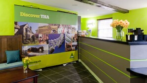 A reception area with a green and grey color scheme, a large 'Discover YHA' poster, a vase with flowers, and a wooden bench. - YHA South Downs - Hostel (Lewes)
