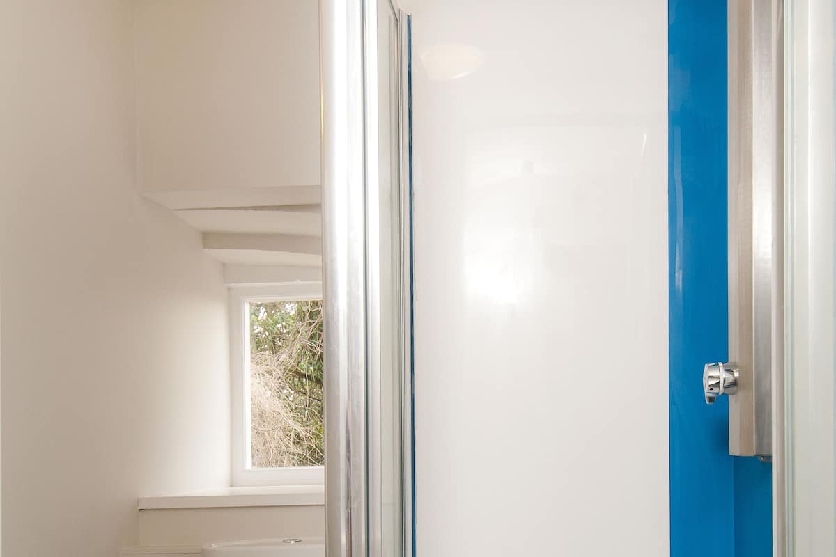 A bathroom with a white toilet, a glass-enclosed shower with a blue accent, and a window above the toilet.
