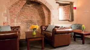 A room with a brick fireplace, leather sofas, a small table with a vase of flowers, and a window with a curtain. - YHA South Downs - Hostel (Lewes)