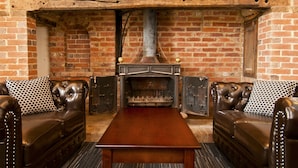 A room with a brick fireplace, leather sofas, and a wooden table. - YHA South Downs - Hostel (Lewes)