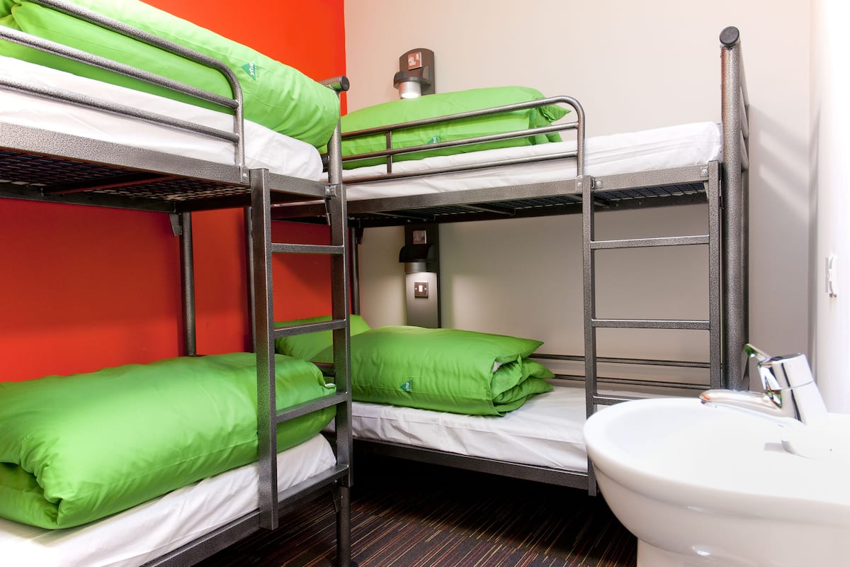A bunk bed room with green bedding and a white sink.