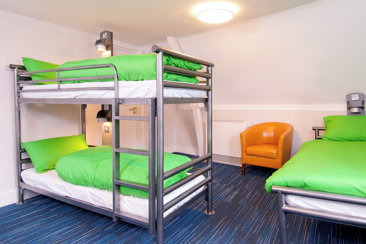 A bunk bed room with green bedding, a blue carpet, and a single orange chair.