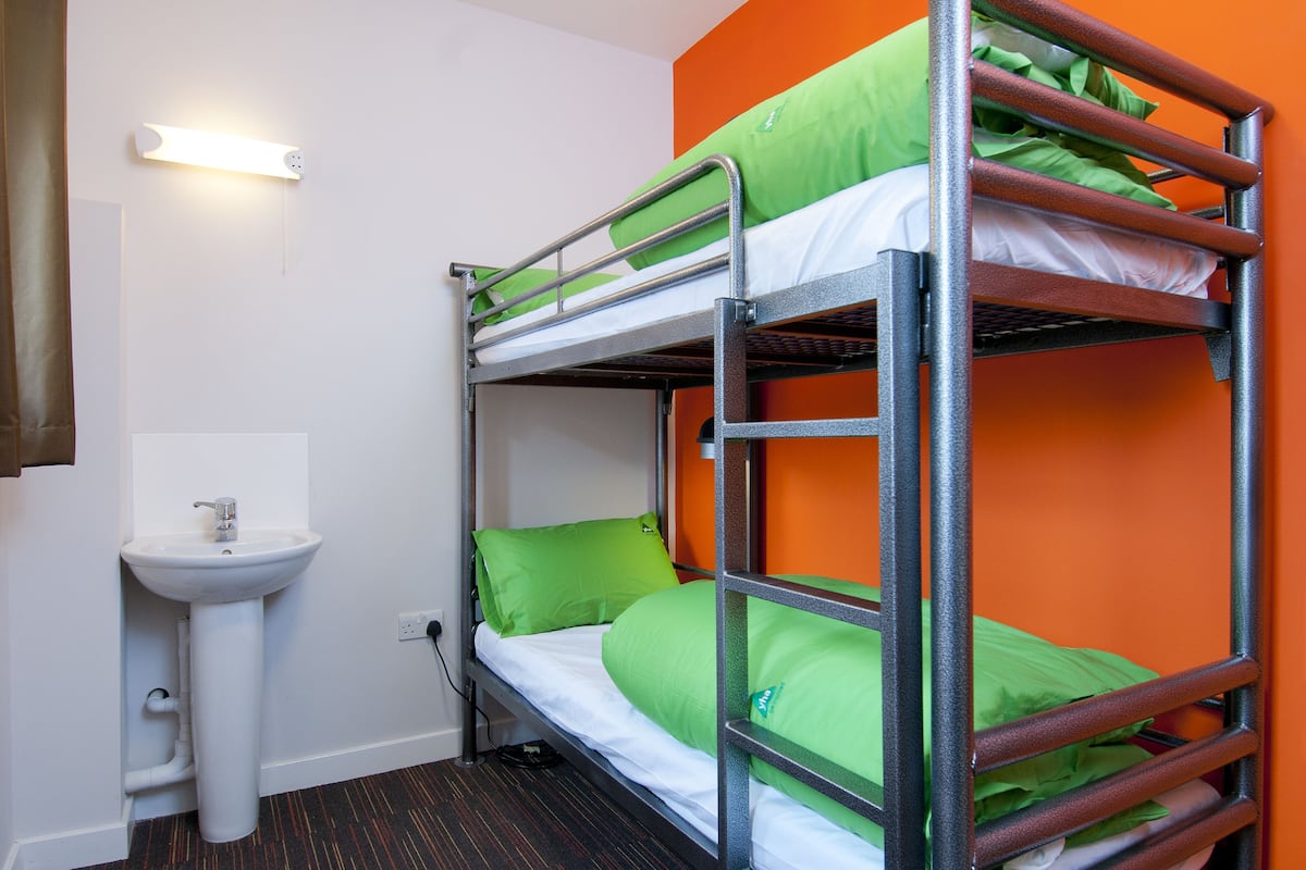 A bunk bed with green bedding, a white sink, and an orange accent wall.