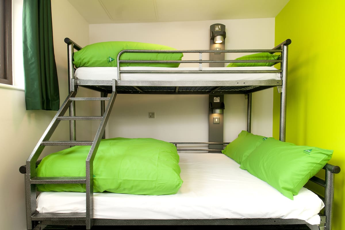 A bunk bed with green pillows and a nightstand with a lamp.