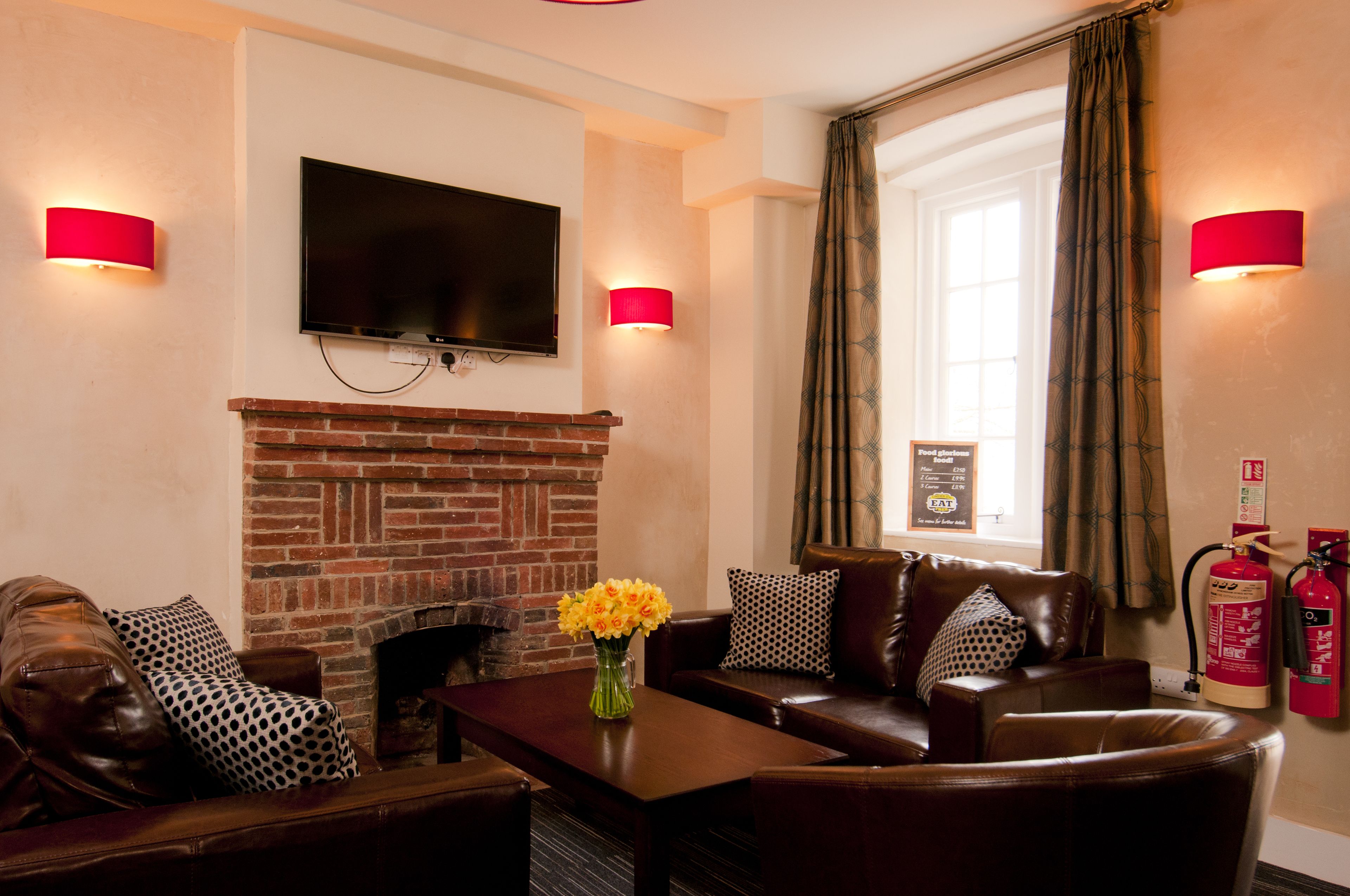A living room with a brick fireplace, leather sofas, a flat-screen TV, and red wall sconces.