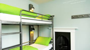 Una cama litera con ropa de cama verde, una lámpara de lectura en la pared y una chimenea.