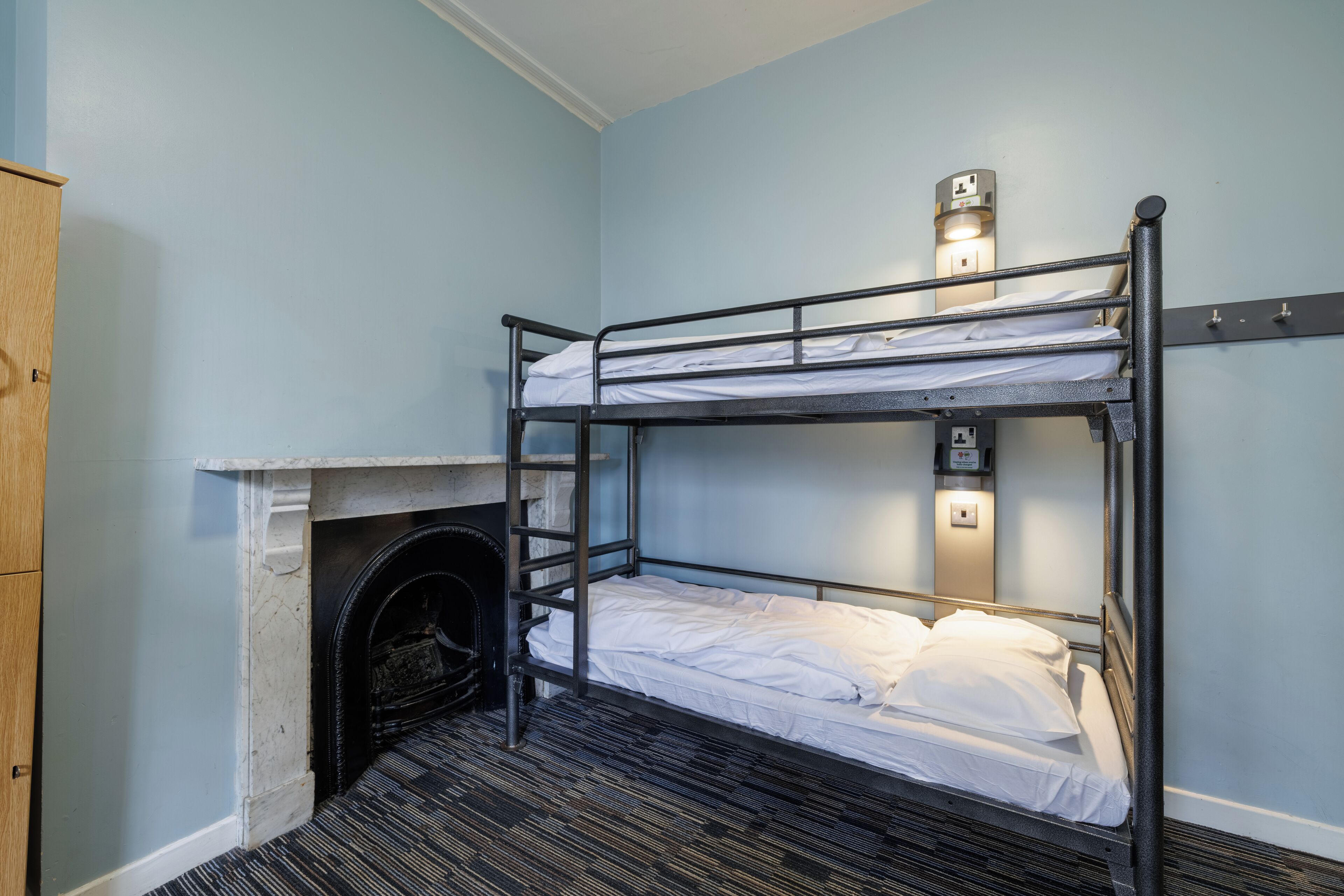 A bunk bed room with a fireplace, a wardrobe, and a wall-mounted light fixture.