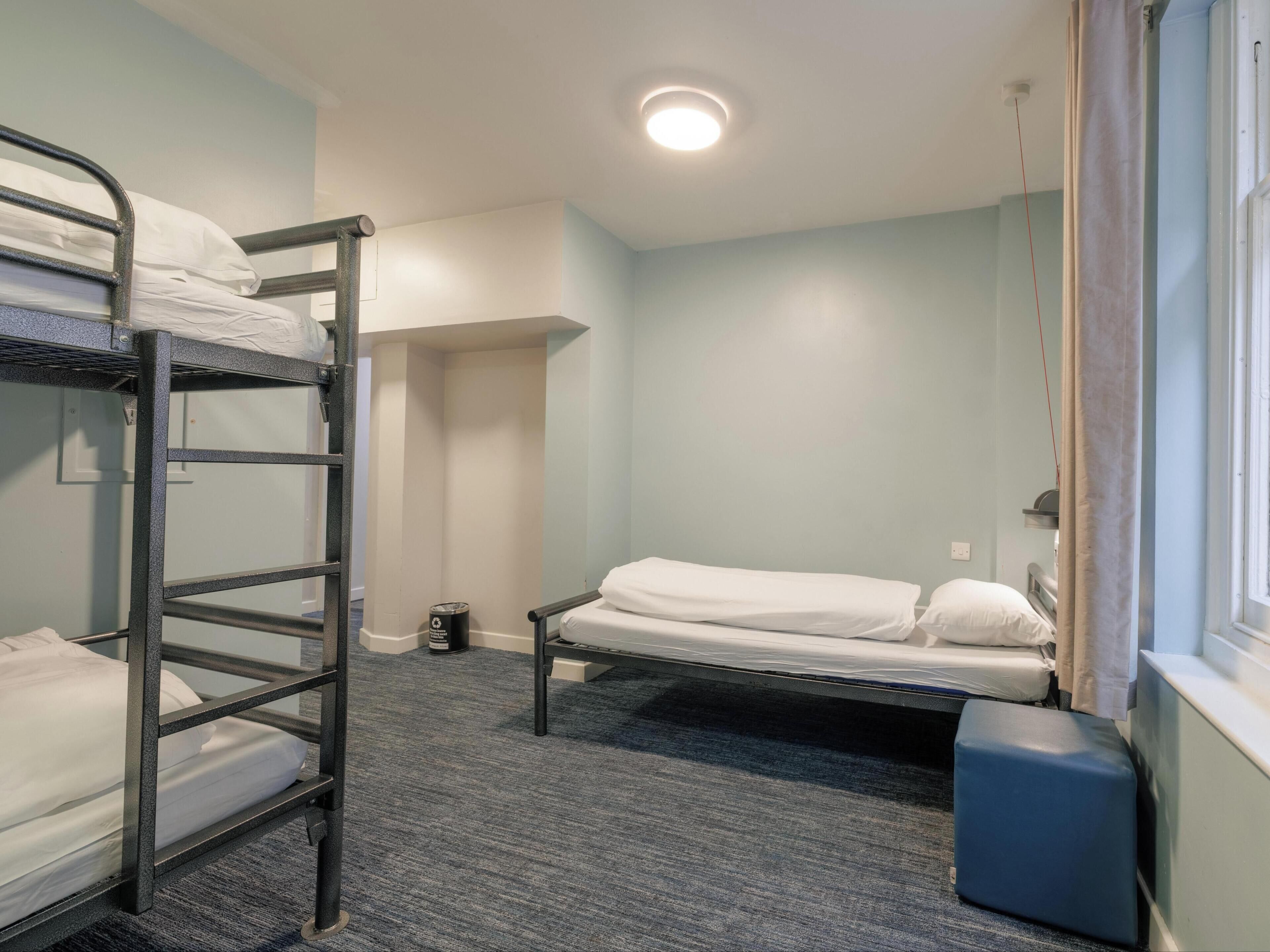 A dormitory room with bunk beds, a small window, and a carpeted floor.