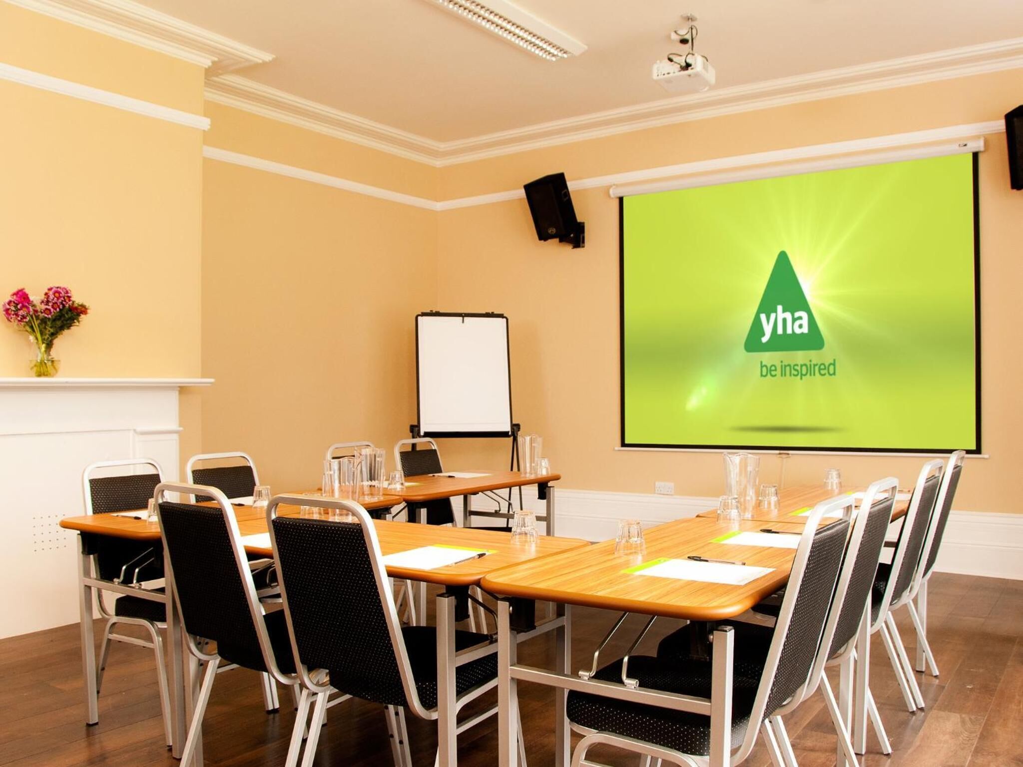 Un salón de conferencias con una pantalla grande que muestra 'yha be inspired', una pizarra y un proyector.