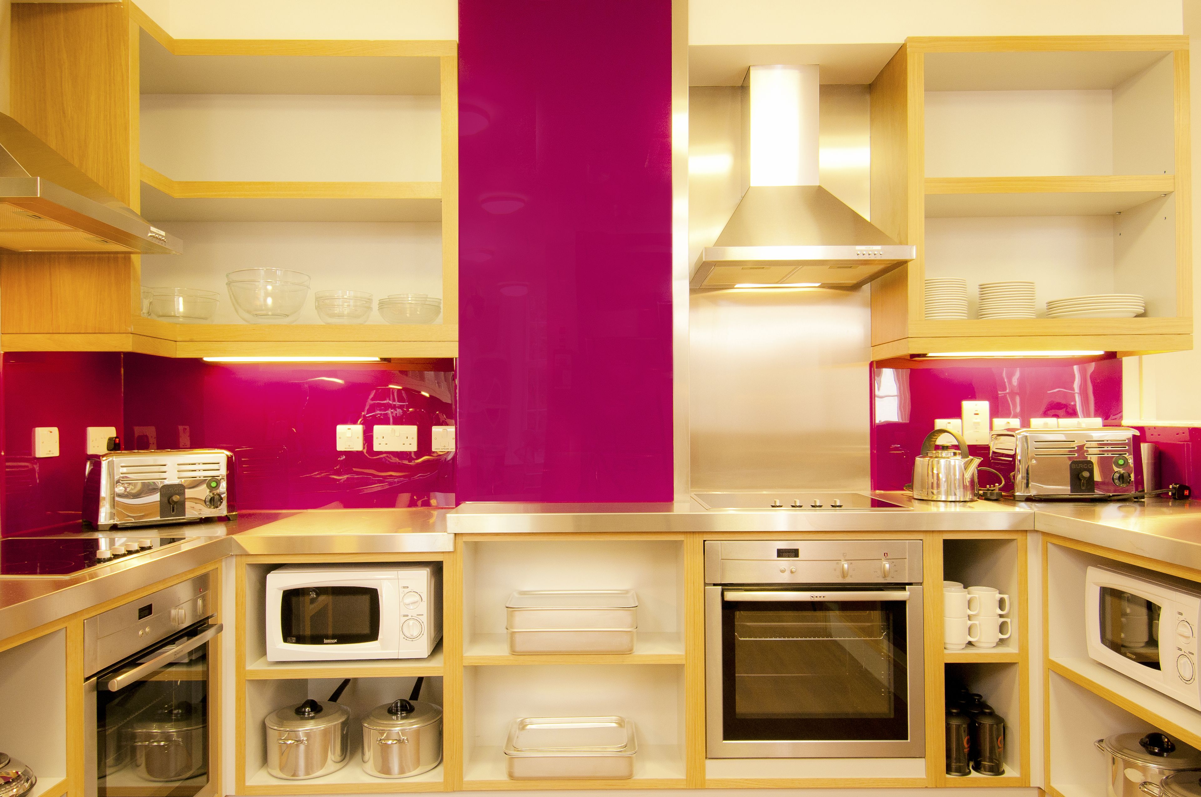 A compact kitchen with built-in appliances, including a microwave, oven, and toaster, and a pink accent wall.