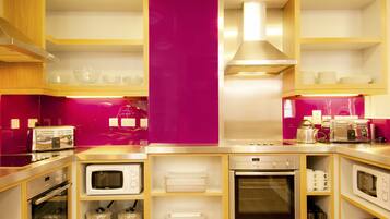 A compact kitchen with built-in appliances, including a microwave, oven, and toaster, and a pink accent wall.