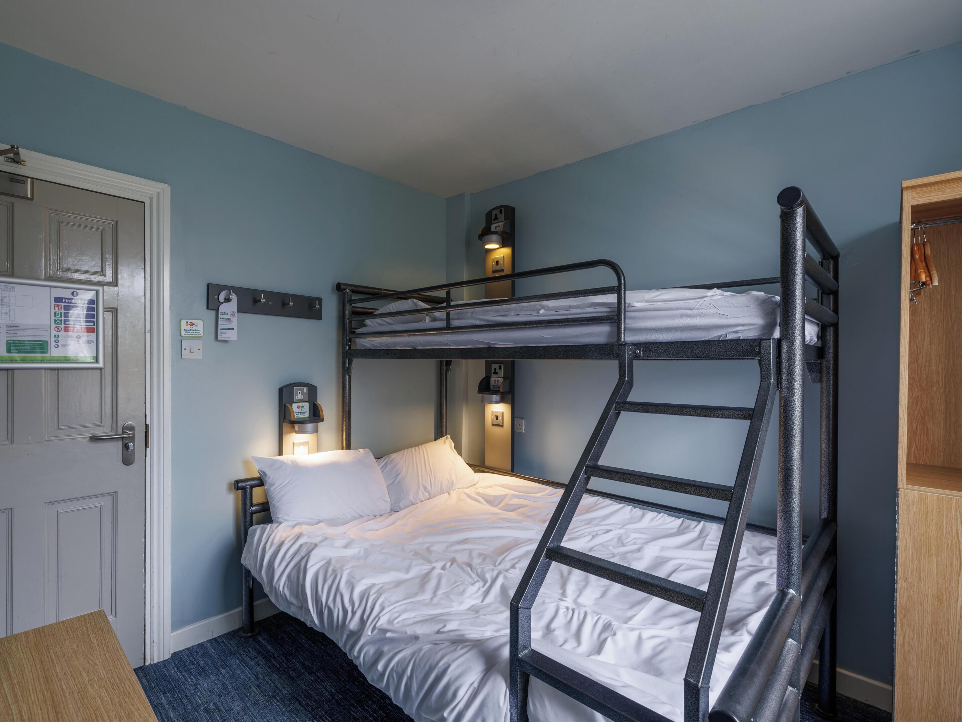 A bunk bed room with a door, a nightstand, a wall-mounted light, and a wooden cabinet.
