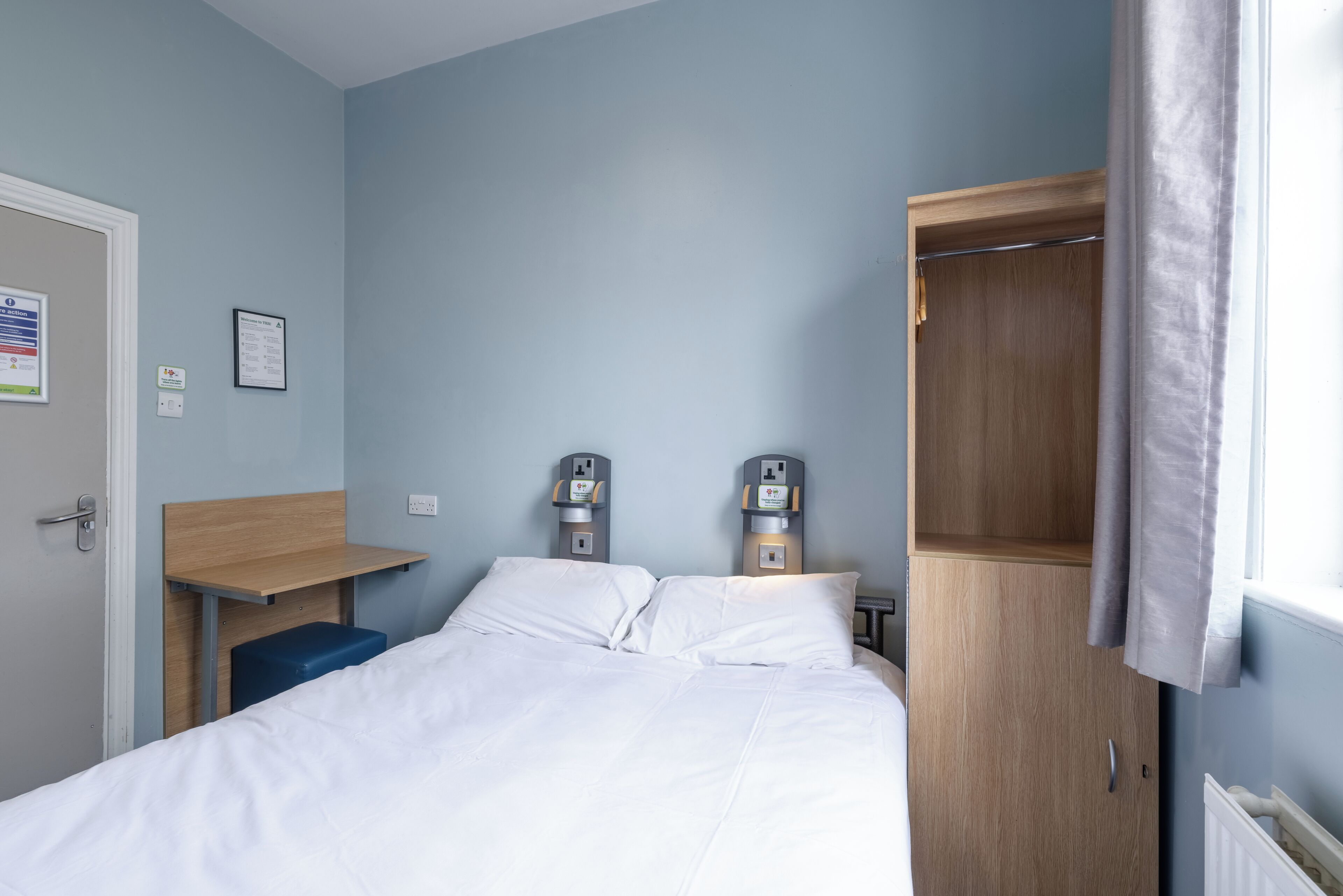 Une chambre d’hôtel équipée d’un lit, d’un bureau, d’une armoire et de deux machines à café fixées au mur.