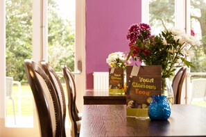 A dining table with chairs, a vase with flowers, and a menu stand. - YHA Stratford-upon-Avon - Hostel (Stratford-upon-Avon)