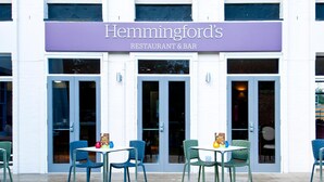 Restaurante y bar Hemmingford con un letrero morado, dos mesas con sillas y una terraza de madera.