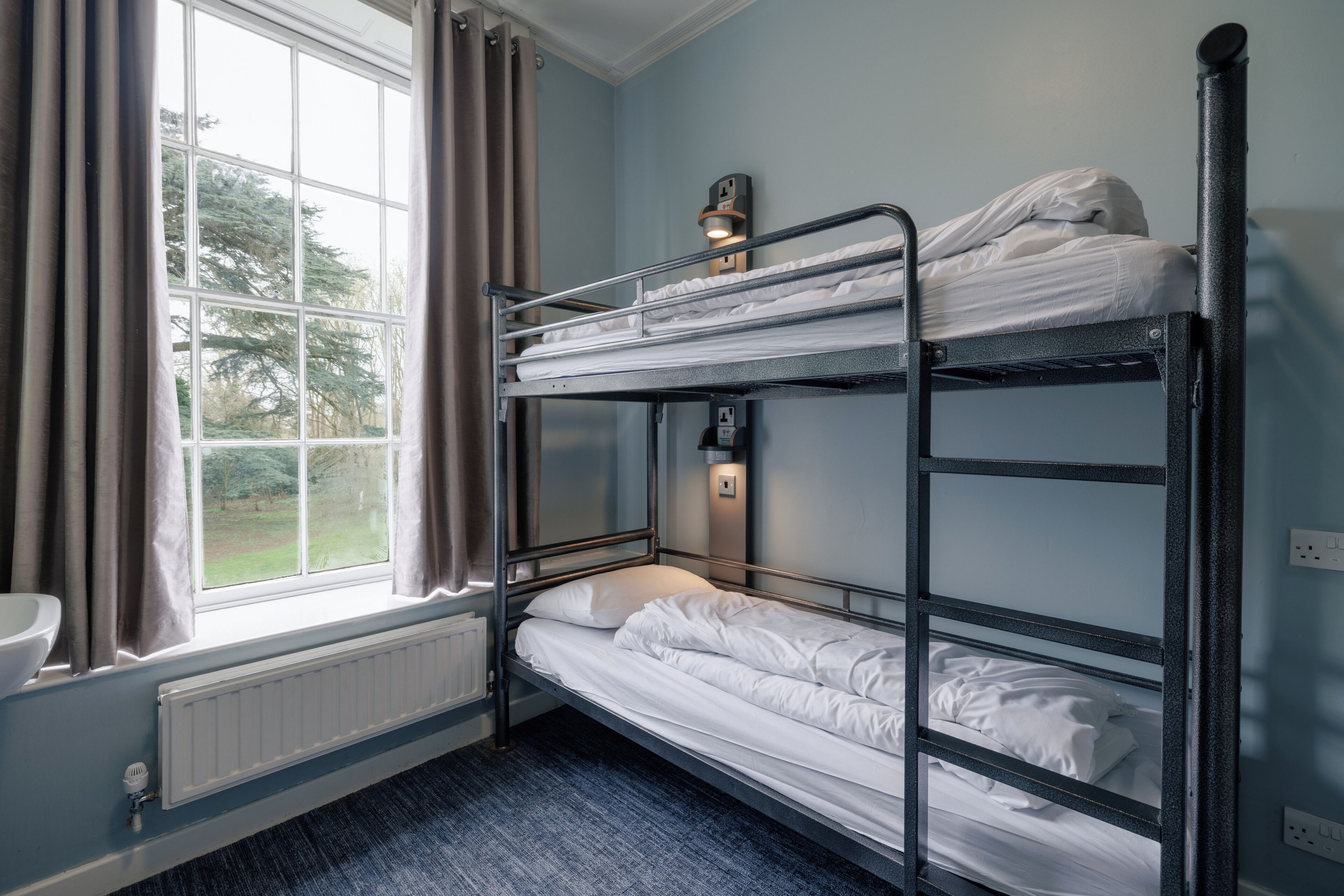 A bunk bed room with a window, radiator, and a wall-mounted light fixture.