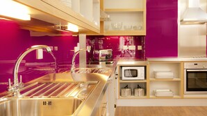 Una cocina moderna con electrodomésticos de acero inoxidable, estantes de madera y una pared de acento rosa brillante.