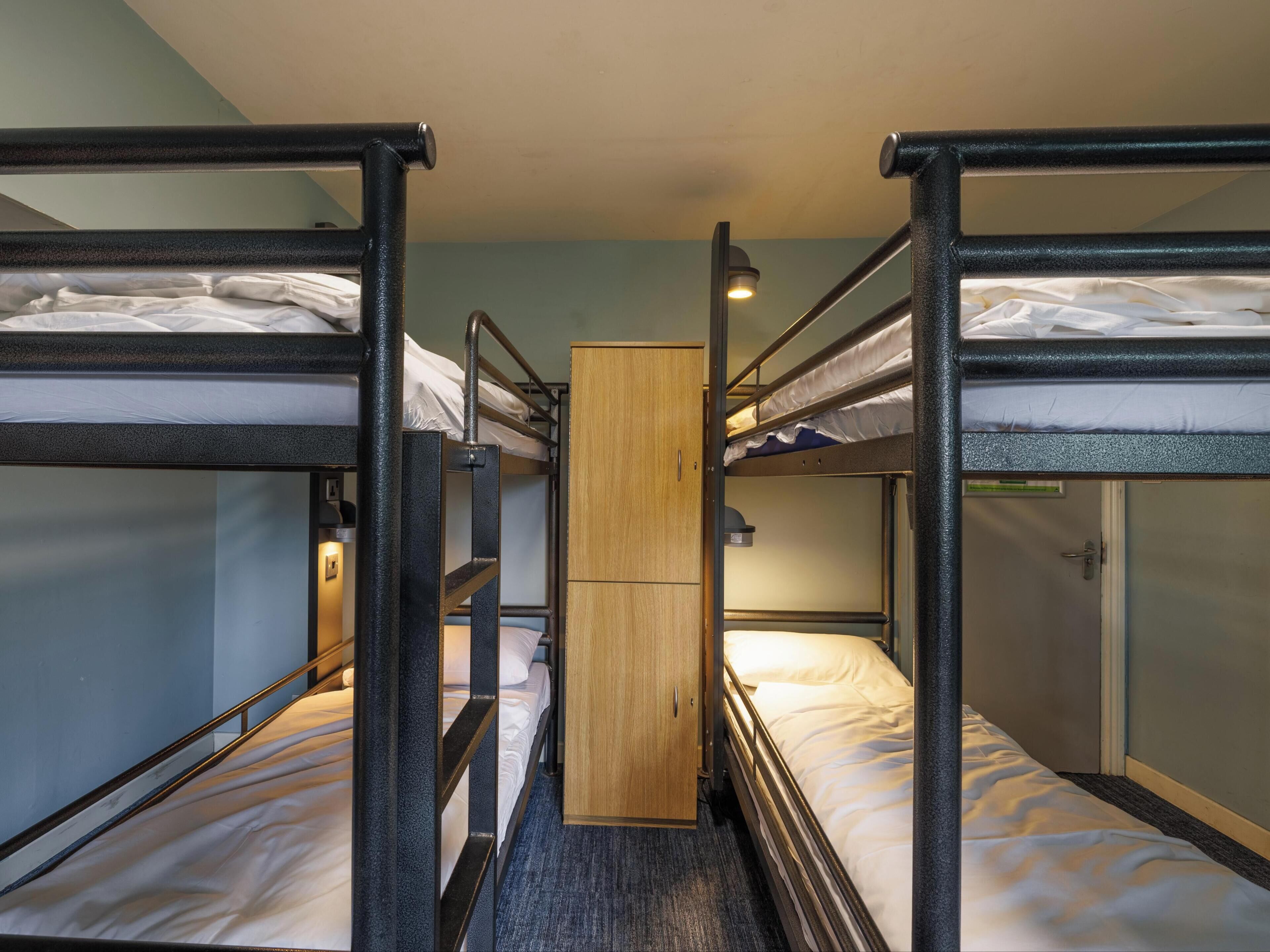 Habitación con literas, un mueble central de madera, barandillas metálicas y piso alfombrado.