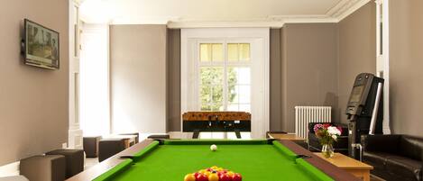 Une table de billard avec des billes, un canapé et un radiateur dans une pièce avec une fenêtre et un tableau accroché au mur.