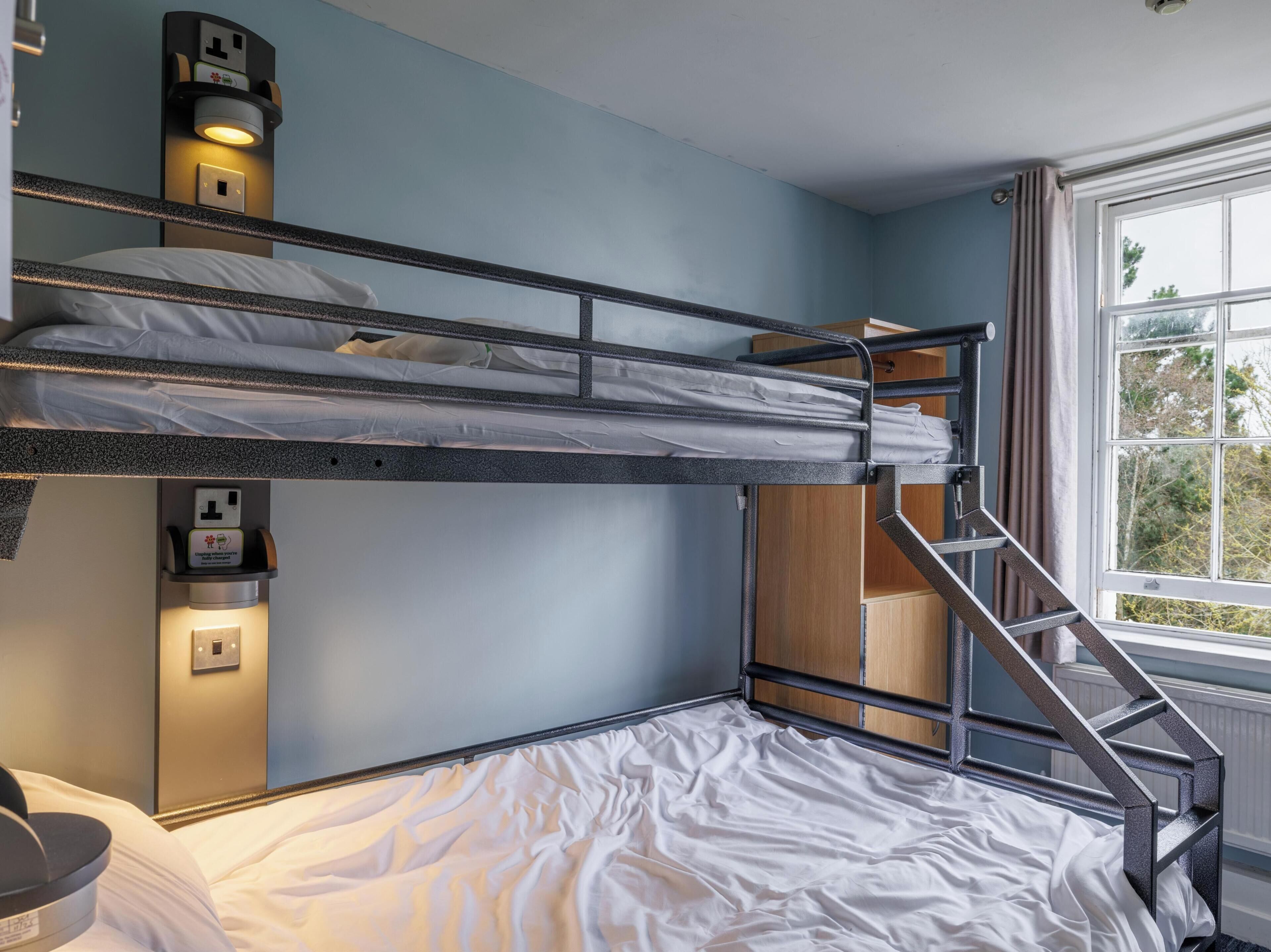 Habitación con literas, una ventana, un escritorio y un estante pequeño con luz.