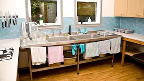 A kitchen with a large stainless steel sink, a stove, and wooden cabinets. - YHA Streatley - Hostel (Reading)