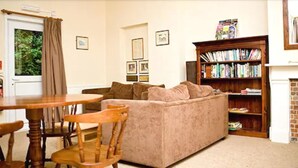 A living room with a beige sofa, wooden chairs, a round table, a bookshelf, and a fireplace. - YHA Streatley - Hostel (Reading)