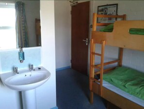 A bunk bed with a green sheet, a white sink, and a mirror in a room with a door and a framed picture on the wall. - YHA Streatley - Hostel (Reading)